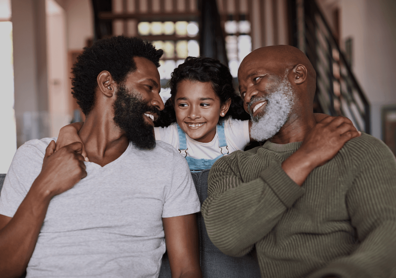 Three family members sitting close together, one embracing the other, in a cozy indoor setting.