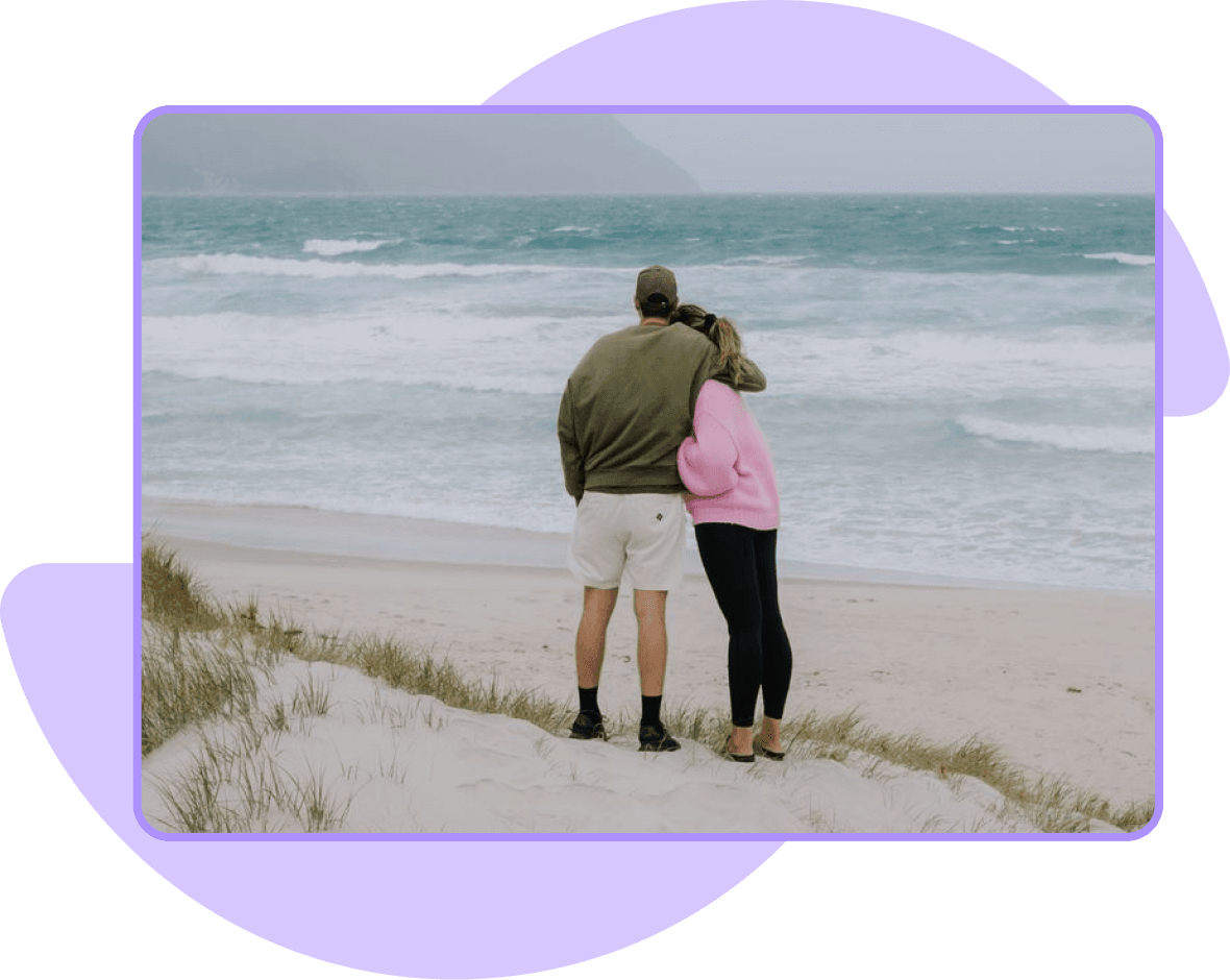 A couple embracing while looking at a wavy sea from a sandy beach